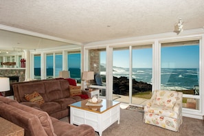 Enjoy a panoramic ocean view from the large window in this comfortable living room with a sofa, coffee table, and armchair.