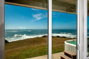 Blick auf den Ozean durch eine Glastür, mit Whirlpool und einer Holzbank.