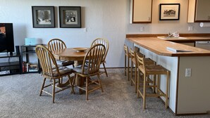 Cozinha compacta com área de jantar, apresentando mesa e cadeiras de madeira, uma pequena ilha com banquetas e uma máquina de lavar louça embutida.