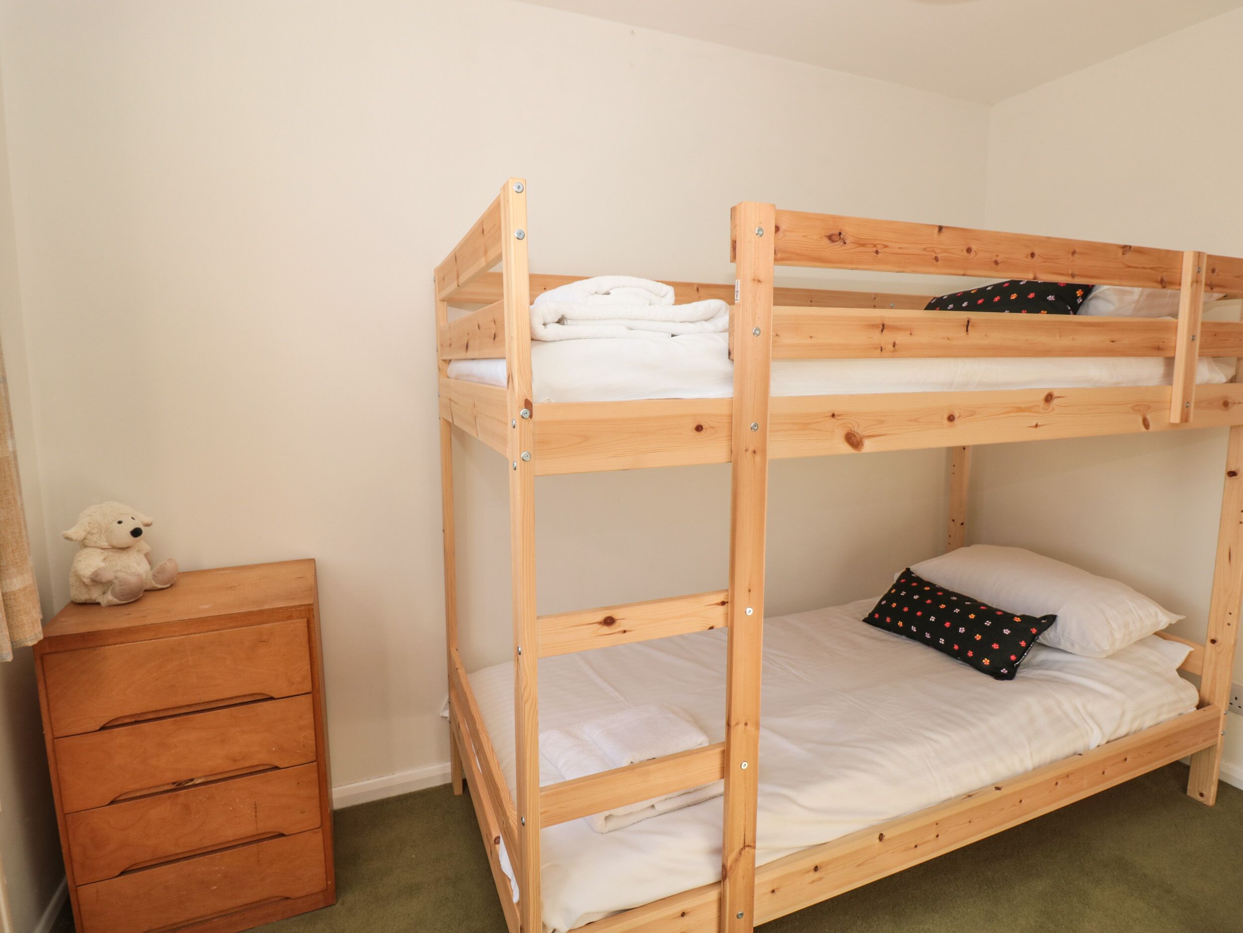 A bunk bed with a wooden frame, a small wooden dresser, and a teddy bear on the dresser.