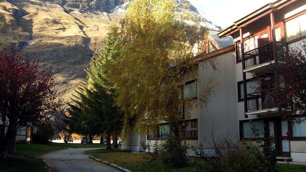 A building with a balcony, a mountain in the background, and a tree in the foreground. - 4-PERSON STUDIO AT THE FOOT OF THE NORDIC SKI SLOPES (BESSANS)