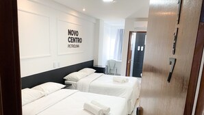A hotel room with two beds, a desk, and a chair. There is a sign on the wall that reads "NOVO CENTRO PETROLINA".