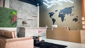 A modern reception area with a world map on the wall, a green wall with plants, and a black rug.