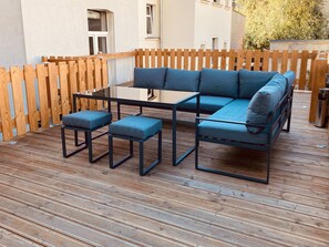 Uma área de estar moderna ao ar livre, com mesa de vidro e assentos acolchoados em azul.