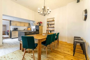 Uma cozinha moderna com armários de madeira, uma ilha central e uma área de jantar com mesa de madeira e cadeiras verdes.