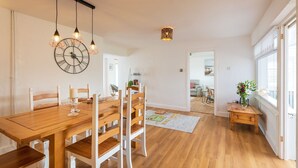 Een ruime eetruimte met een houten tafel en stoelen, een wandklok en hanglampen.