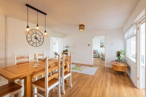 A dining area with a wooden table and chairs, a wall clock, pendant lights, and a view into another room. - Faraway: Pet-friendly holiday home for 6 in Rhosneigr (Rhosneigr)