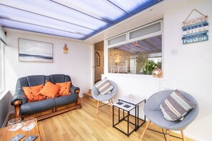 A cozy living room with a sofa, armchair, and coffee table, a window with a view, and a wall with decorative items. - Faraway: Pet-friendly holiday home for 6 in Rhosneigr (Rhosneigr)