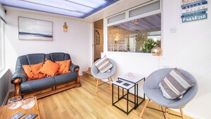 Een gezellige woonkamer met een leren bank, een grijze fauteuil en een kleine tafel met glazen.