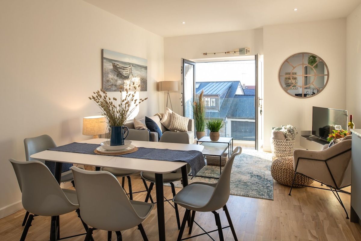A modern living room with a dining area, a sofa set, a TV, and a large window offering a view of the outside.