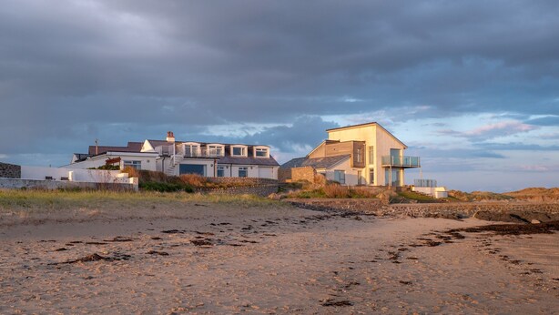 Una propietat a la costa amb una casa moderna, una platja al primer terme i un cel nuvolós.