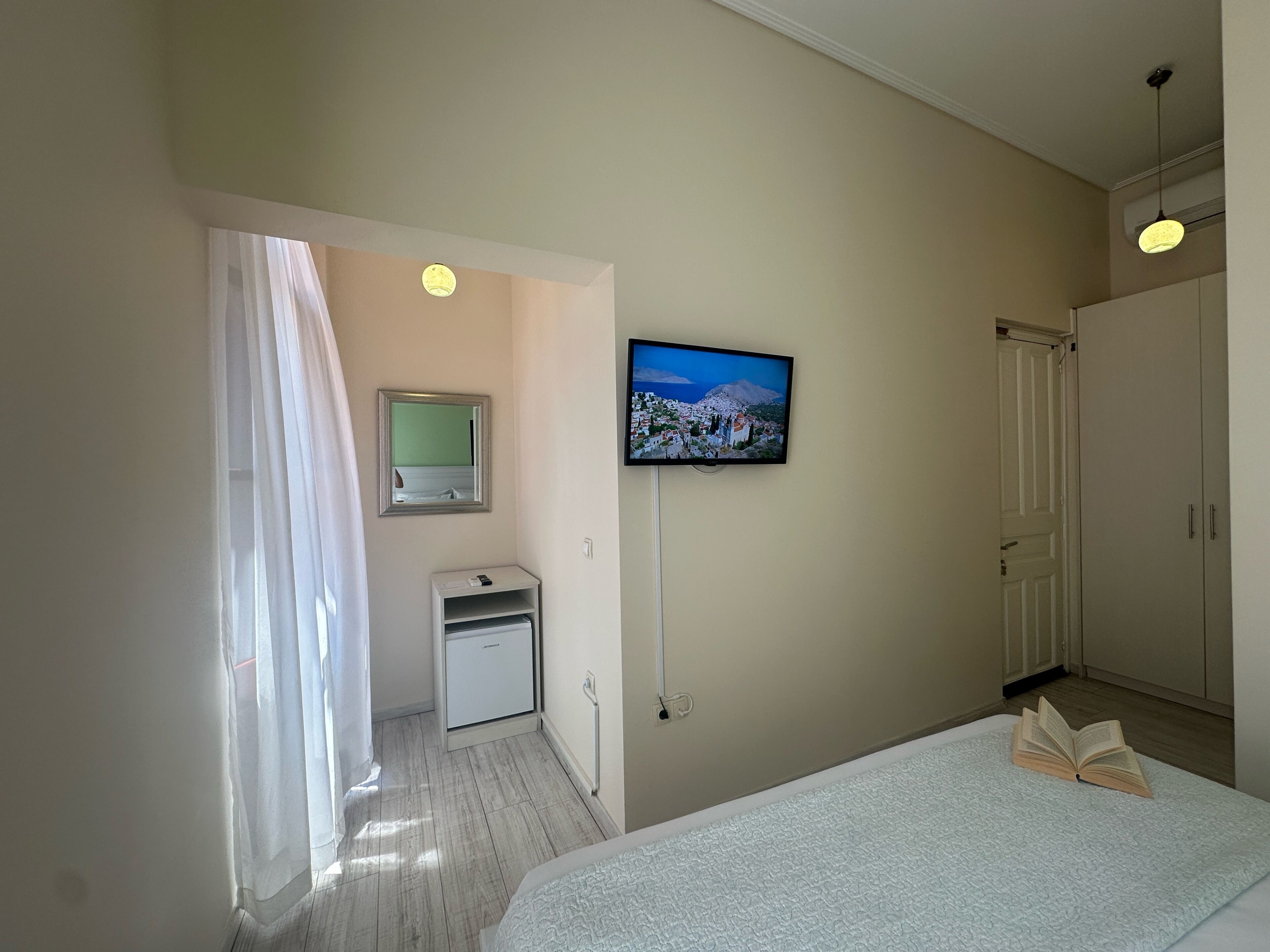 A hotel room with a bed, a television mounted on the wall, a small desk, and a door leading to another room.