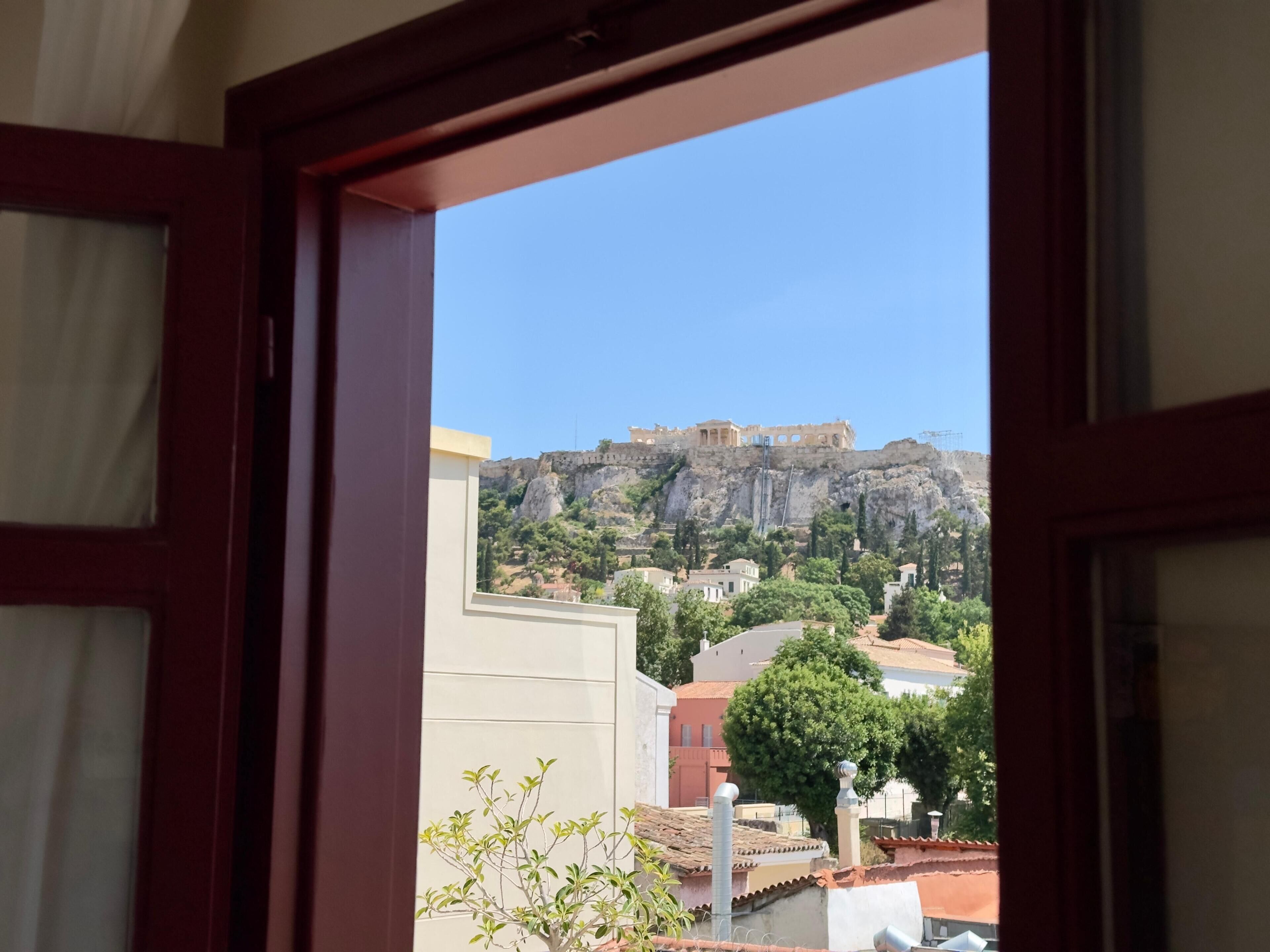 Une vue à travers une porte ouverte d’un bâtiment, donnant sur un site historique avec des ruines situées sur une colline.