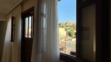 A room with a view of a hill and buildings, a window with curtains, and a door.