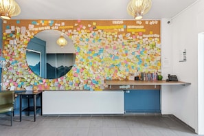 A reception desk with a corkboard covered in colorful notes, a mirror, and a small selection of books and a phone.