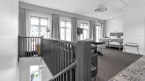 Et moderne hotelværelse med balkon, store vinduer, et fladskærms-tv, en sofa og et spiseområde.