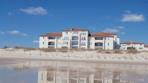 A beachfront property with a reflective pool, multiple balconies, and a sandy beach in the background.