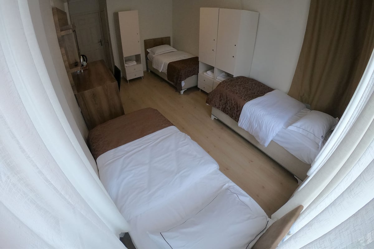 Una habitación de hotel compacta con dos camas individuales, un armario, un escritorio y un espejo.