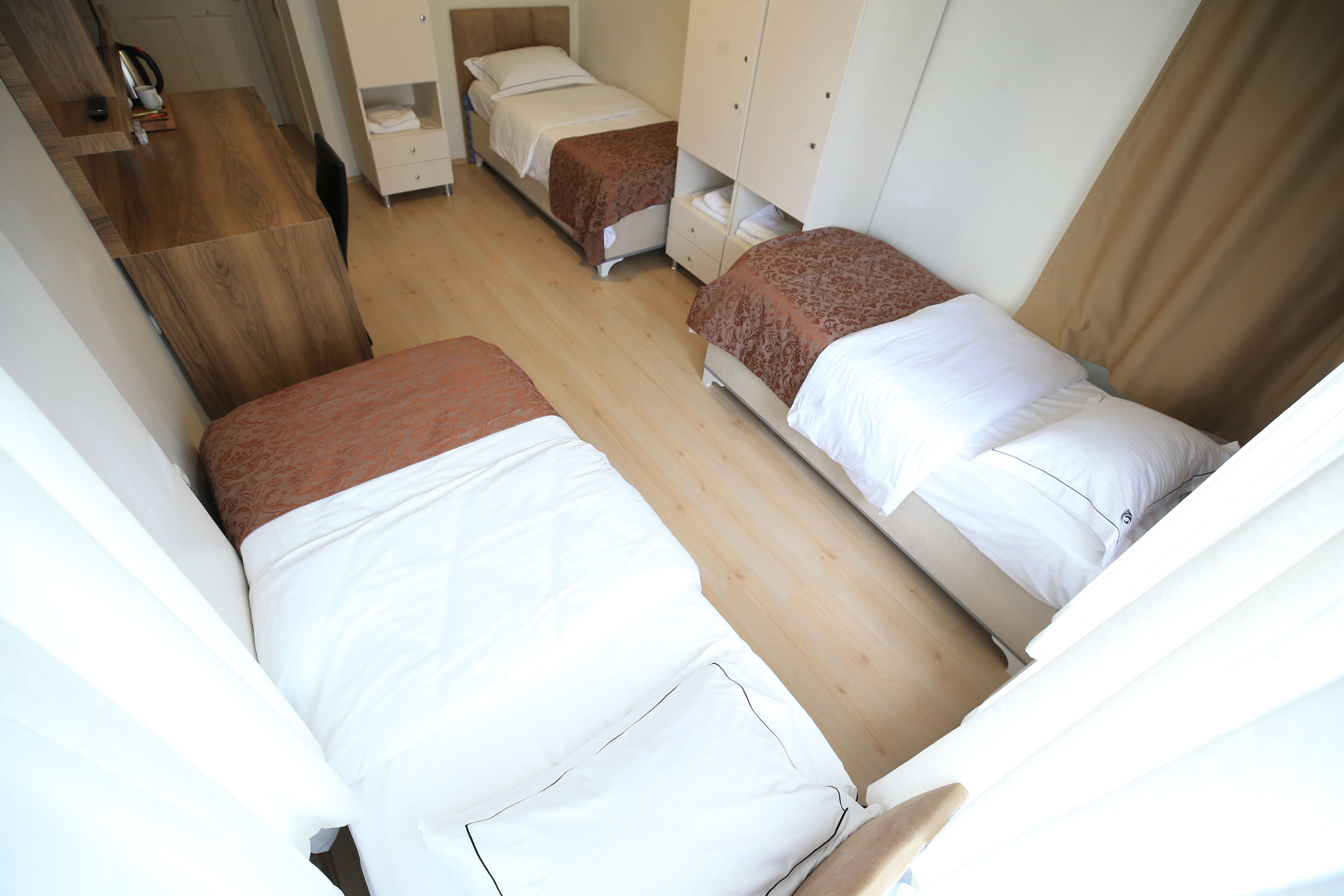 A hotel room with two single beds, a wooden desk, and a wardrobe.