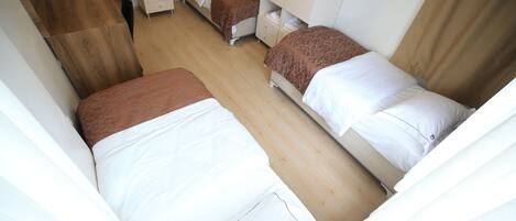Quarto de hotel com duas camas de solteiro, uma escrivaninha de madeira e um guarda-roupa.