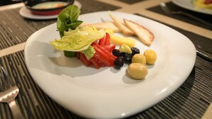 A plate with a variety of food items including lettuce, tomatoes, olives, and cheese, placed on a table with a placemat. - Evim Butik Hotel (Kirklareli)