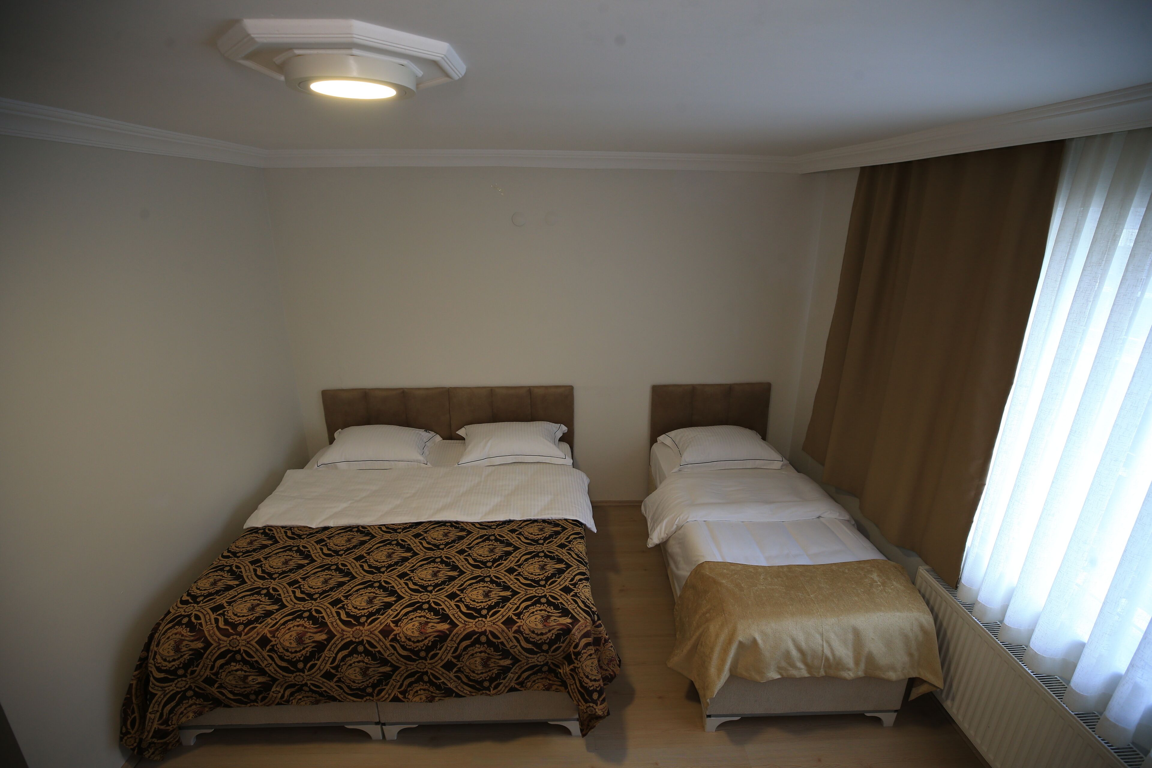 Een tweepersoonskamer met twee bedden, een plafondlamp en een raam met gordijnen.