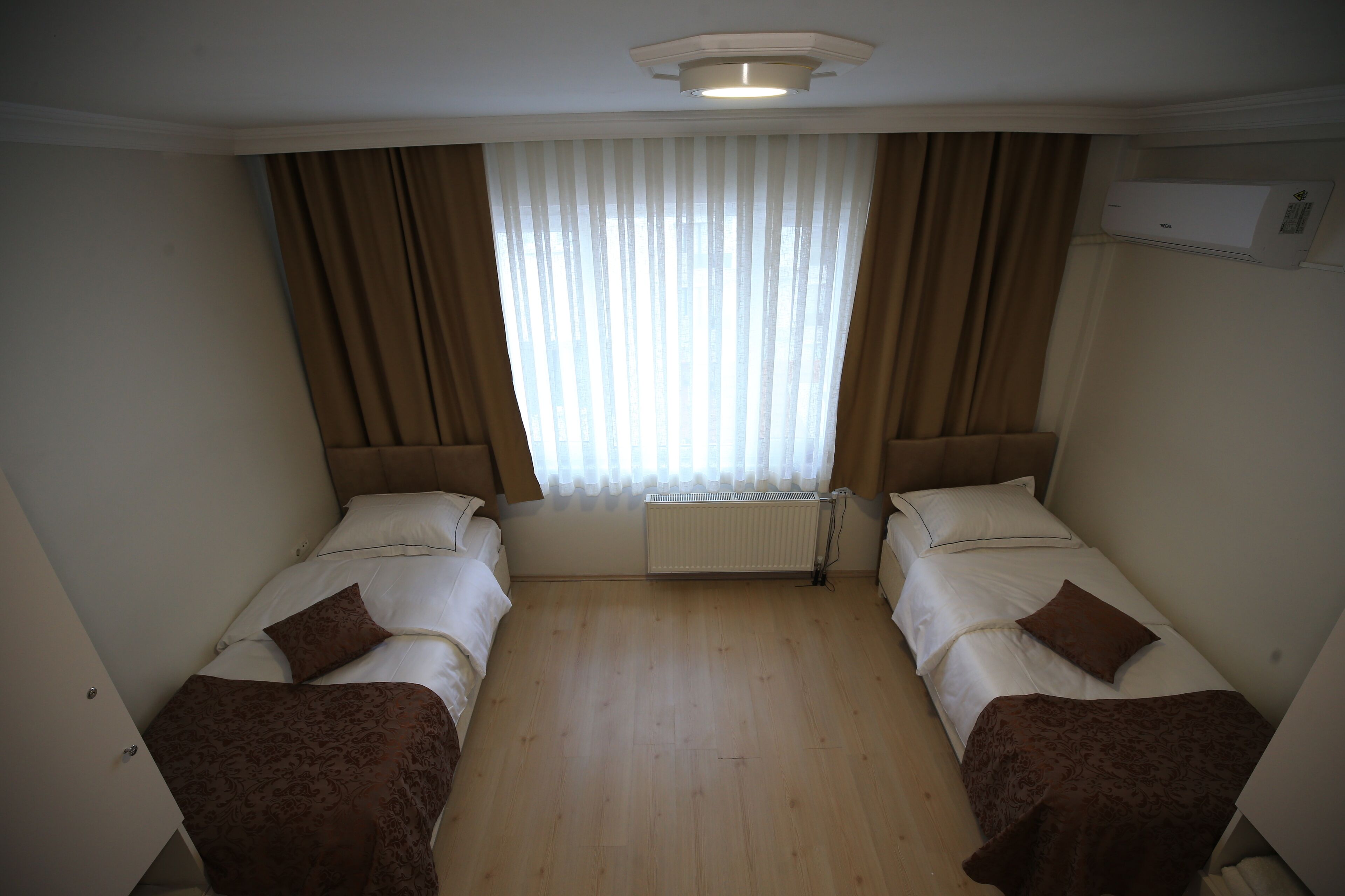 Habitación de hotel con dos camas individuales, un radiador, una ventana con cortinas y un equipo de aire acondicionado.