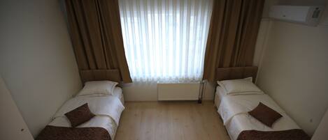 Habitación de hotel con dos camas individuales, un radiador, una ventana con cortinas y un equipo de aire acondicionado.