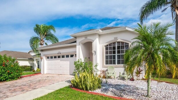 A single-story house with a garage, a well-maintained lawn, and a small garden area with plants and a chair. - "southern Charm" 4 Bed & 2 Bath Private Pool Home 4 Bedroom Villa by RedAwning (Davenport)