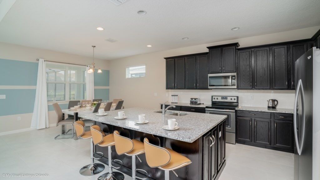 A modern kitchen with dark cabinets, a large island with bar stools, and a dining area with a table and chairs.
