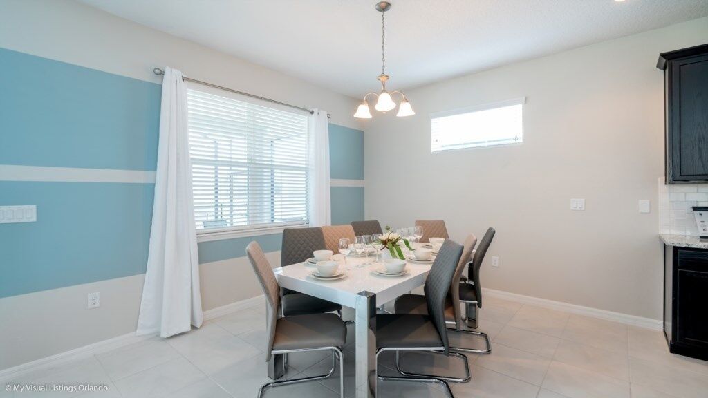 Een eethoek met een tafel voor vier personen, een raam met zonwering en een keuken met een vaatwasser.