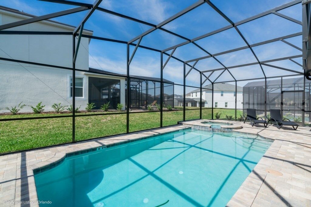 A swimming pool with a clear view of the surrounding area, including a house and a grassy lawn.