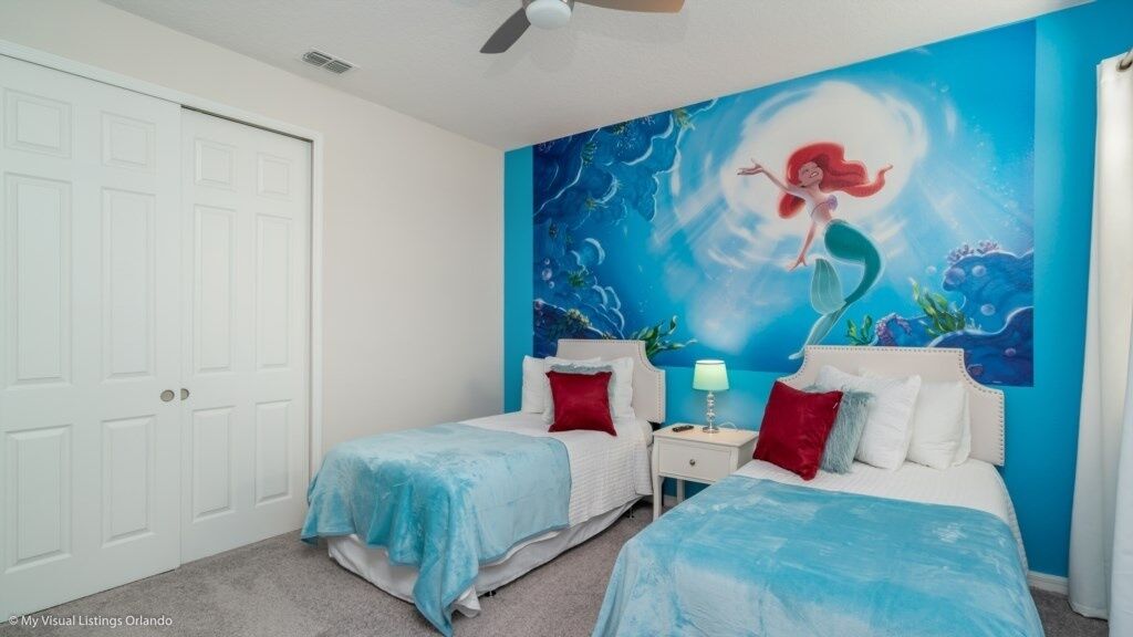 A bedroom with two beds, a mural of a mermaid on the wall, and a ceiling fan.
