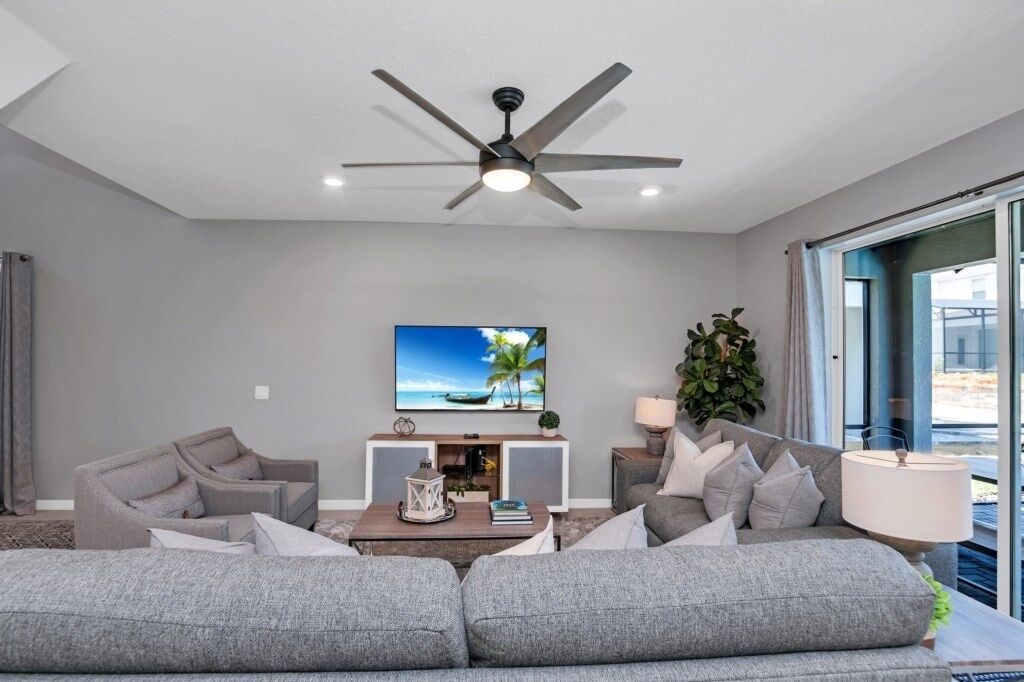 Una sala de estar moderna con un sofá gris, una mesa de centro, un televisor y un ventilador de techo.