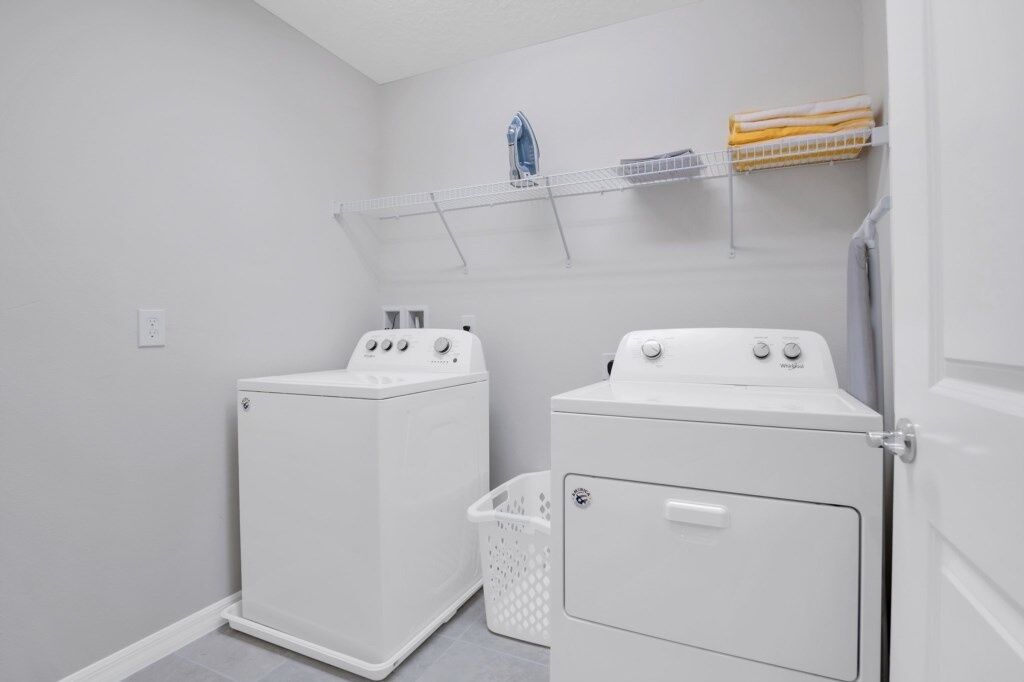 A laundry room with two white washers and dryers, a metal drying rack, and a white basket.