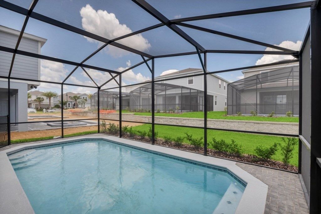 A swimming pool with a glass enclosure, surrounded by a landscaped area and residential buildings in the background.