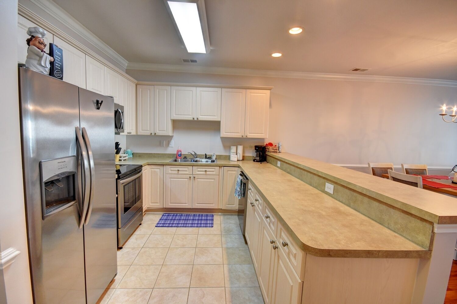 A modern kitchen with stainless steel appliances, light-colored cabinets, a central island, and a dining area with chairs.