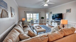 A spacious living room with a large sectional sofa, a flat-screen TV, and a ceiling fan. - 4827 Magnolia Lake Drive, #302 3 Bedroom Condo by RedAwning (Myrtle Beach)
