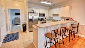 A modern kitchen with white cabinets, a stainless steel refrigerator, a microwave, and a coffee bar with stools. - 4827 Magnolia Lake Drive, #302 3 Bedroom Condo by RedAwning (Myrtle Beach)