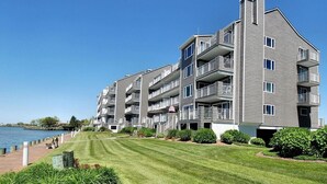 A multi-story residential building with balconies, a grassy lawn, and a waterfront view. - Harbour Island 403l 2 Bedroom Condo by RedAwning (Ocean City)
