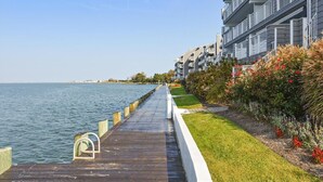 A wooden boardwalk leading to a body of water, flanked by a row of modern buildings with balconies. - Harbour Island 403l 2 Bedroom Condo by RedAwning (Ocean City)