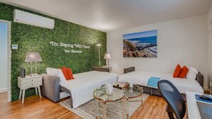 A hotel room with two beds, a desk, a chair, a small table, and a green wall with a text.