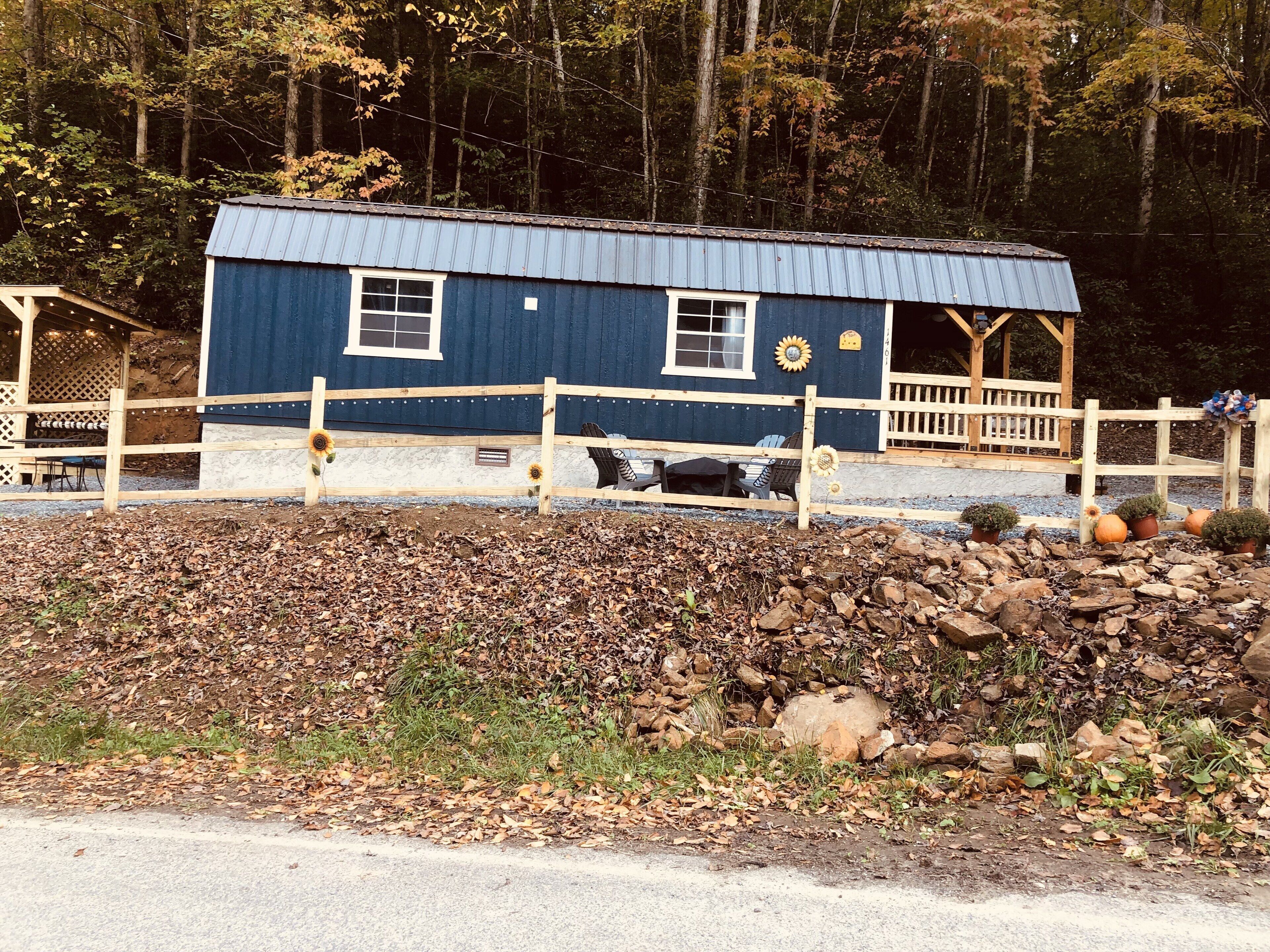 Une cabane rustique à l’extérieur bleu, dotée d’un porche en bois et d’un espace clos agrémenté de plantes en pot.