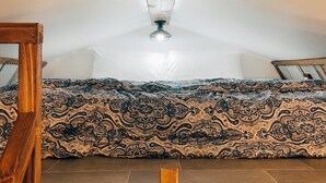 Ein Schlafzimmer im Loft-Stil mit schrägem Dach, einer gemusterten Bettdecke und Holzboden.
