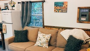Ein gemütliches Wohnzimmer mit einer braunen Couch, einem Fenster mit Vorhängen, einem Kühlschrank und einem an der Wand befestigten Schild.