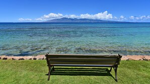 Eine Bank mit Blick auf den weiten, klaren Ozean, im Hintergrund ein Berg.