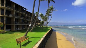 Ein Strandhotel mit mehreren Balkonen, einer Rasenfläche und einer Bank.