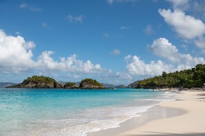 Una playa con agua turquesa cristalina, orilla de arena y islas rocosas con vegetación.