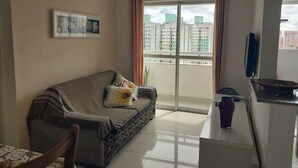 Un salon avec un canapé, une petite table, un téléviseur et un balcon offrant une vue sur la ville.