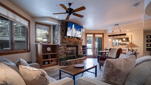 A cozy living room with a stone fireplace, a ceiling fan, and a dining area with a table and chairs. - CX326 | Gorgeous Décor/Flooring | Ski In/out | Winter Shuttle | Hot Tub (Steamboat Springs)